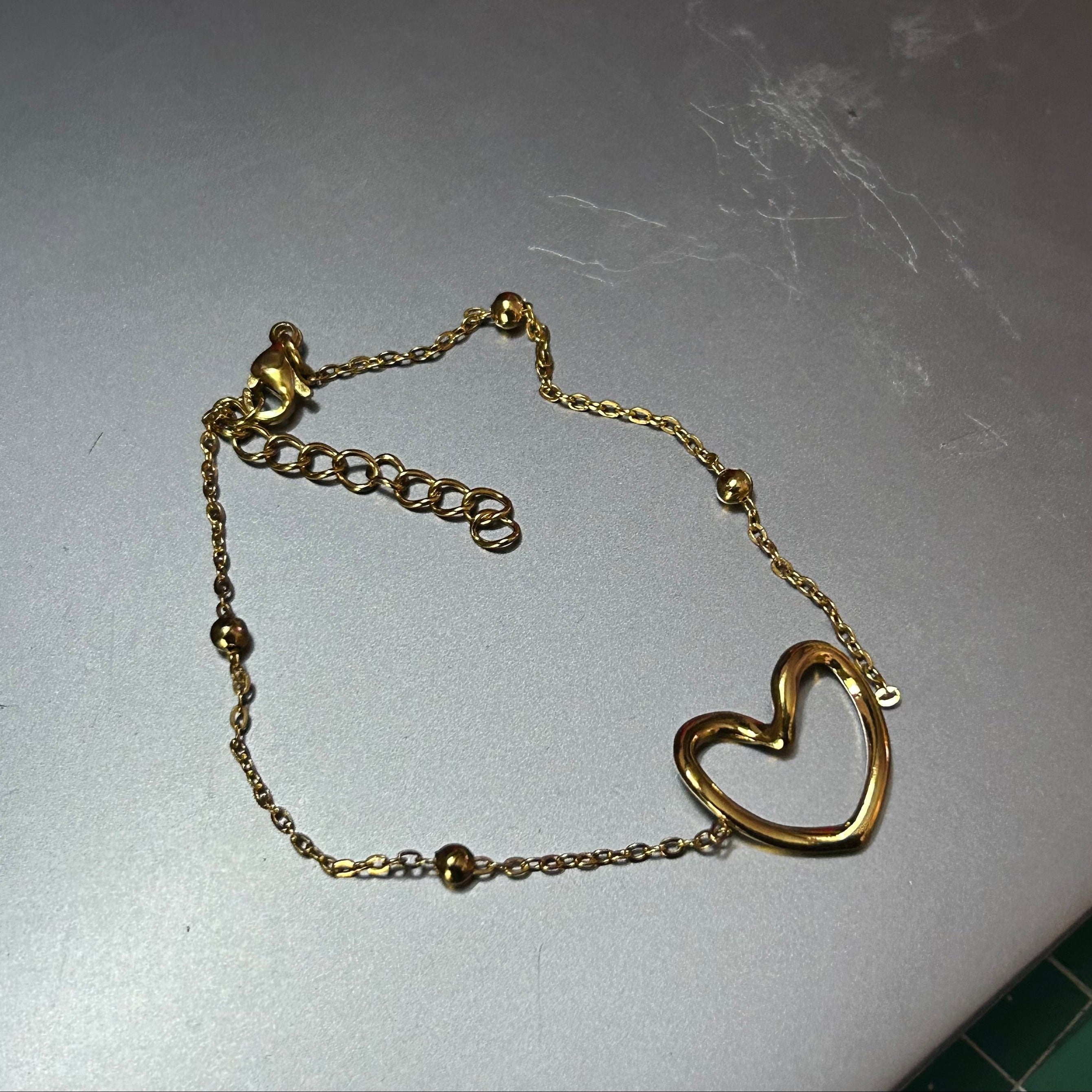 Gold heart-shaped bracelet on a light gray surface