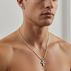 Man wearing a silver necklace with a cross pendant on a neutral background