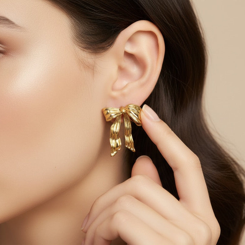 Woman wearing a gold bow-shaped earring against a beige background